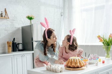 Tavşan kulaklı mutlu anne ve kız Paskalya yumurtalarının yanında birbirlerine bakıyorlar.