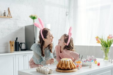 Tavşan kulaklı mutlu anne ve kız Paskalya pastasının yanında birbirlerine bakıyorlar. 