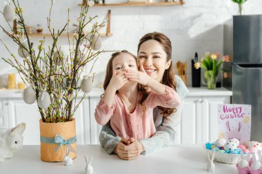 Çocuğun ağzı annesinin yanında, paskalya yumurtaları, söğüt ağacı ve dekoratif tavşanlar. 