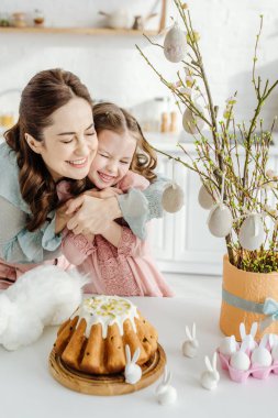 Mutlu bir anne Willowin 'in çiçek saksısı, dekoratif tavşanlar ve paskalya pastası yanında kızını kucaklıyor. 