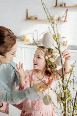 Şaşırmış bir çocuğun söğüt dallarındaki dekoratif paskalya yumurtalarının yanındaki annesine bakması. 