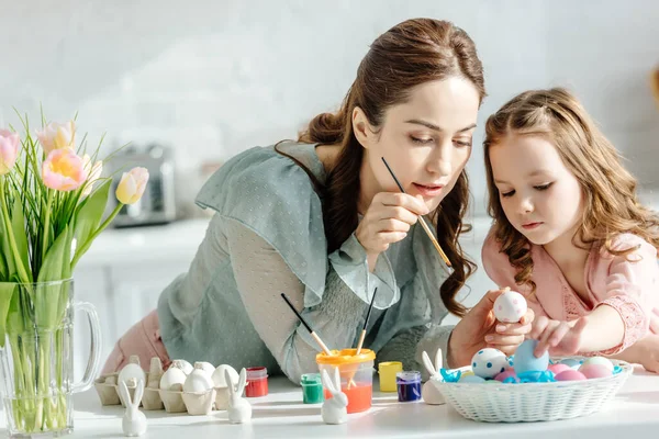 attractive mother and cute daughter painting easter eggs