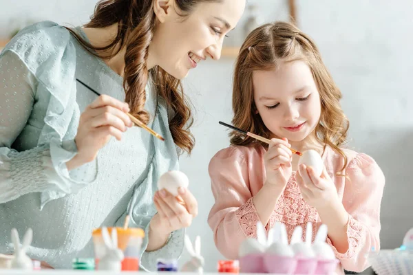 Mãe Atraente Criança Feliz Pintando Ovos Páscoa Perto Coelhos Decorativos — Fotografia de Stock