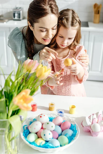 快乐的妈妈和可爱的女儿看着郁金香附近的复活节彩蛋 — 图库照片