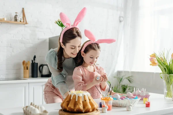 幸せな母親と娘でウサギの耳で見て鶏の卵近くチューリップとイースターパン — ストック写真