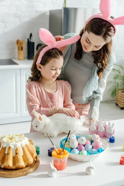 おもちゃのウサギとウサギの耳のかわいい子供の近くの母親 — ストック写真