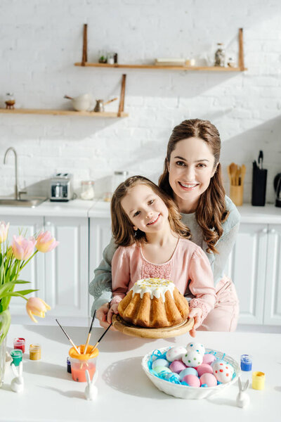 happy child and attractive mother near easter eggs, decorative rabbits, easter bread and tulips 
