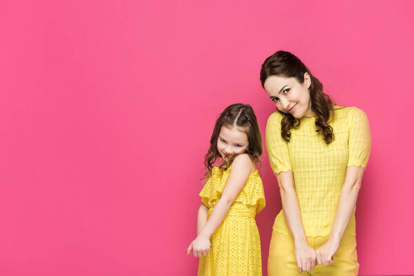 shy mother and daughter looking at camera isolated on pink 