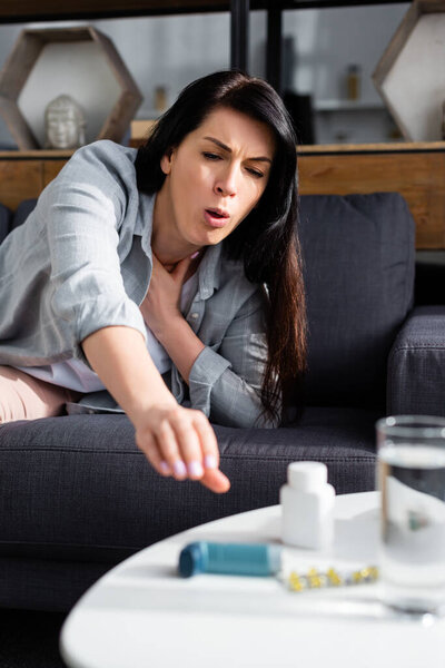 selective focus of woman coughing while reaching for inhaler
