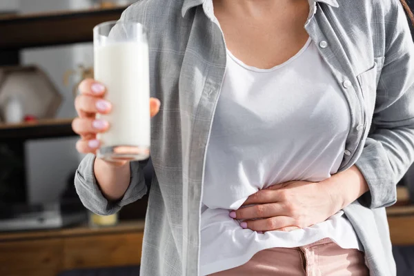 患有乳糖不耐受症的妇女在触摸胃时举着一杯牛奶的剪影 — 图库照片