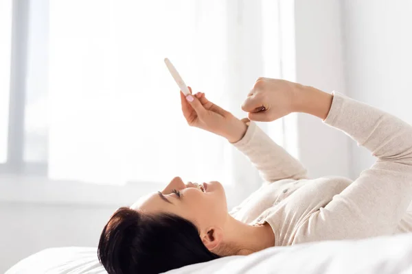 Vrolijk Vrouw Glimlachen Kijken Naar Zwangerschap Test Terwijl Liggend Bed — Stockfoto