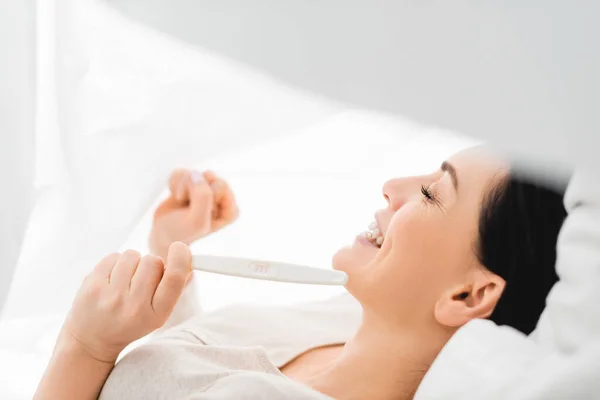 Zijaanzicht Van Positieve Vrouw Kijken Naar Zwangerschapstest Terwijl Liggend Bed — Stockfoto