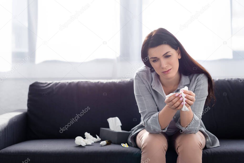 sad woman with allergy holding napkin while sitting on sofa 