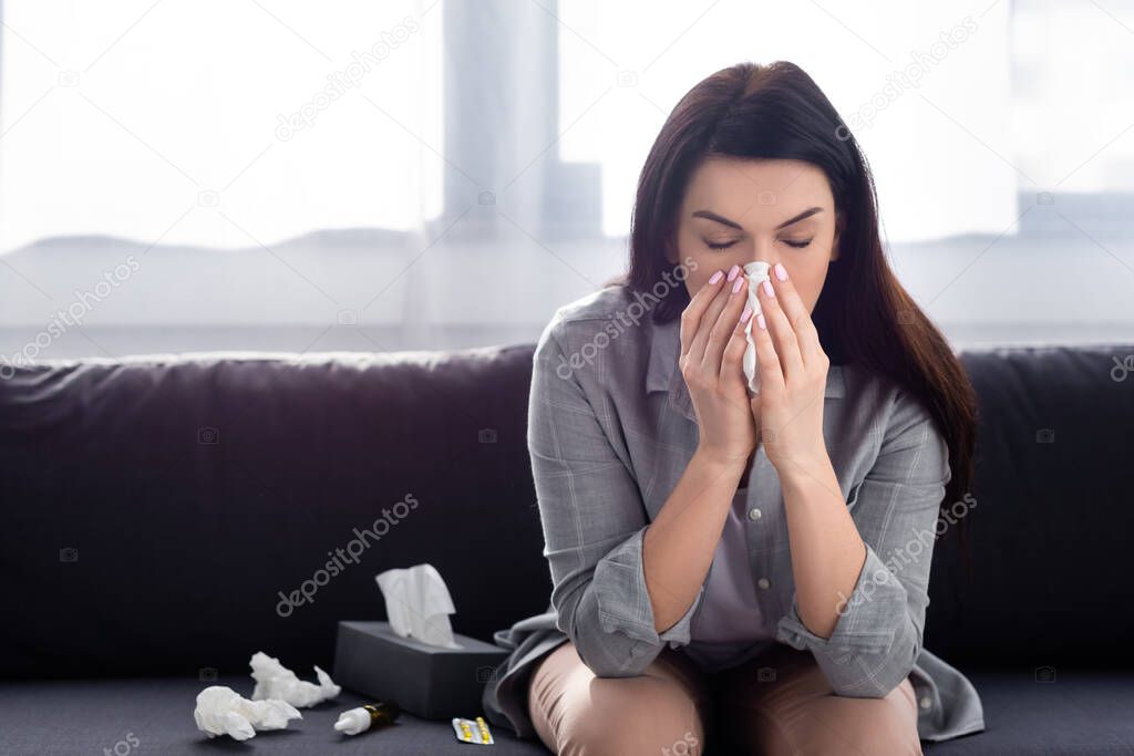 woman with allergy sneezing in napkin while sitting on sofa 