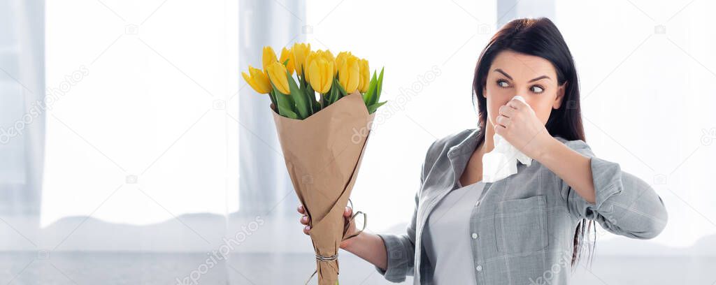 panoramic shot of sneezing woman with pollen allergy looking at tulips 