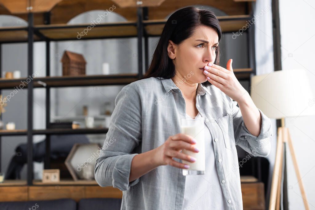 woman with lactose intolerance holding glass of milk and covering mouth 