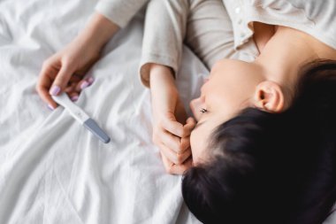 Yatakta hamilelik testinin yanında yatan depresif kadının üst görüntüsü. 