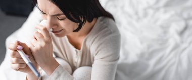 Hüzünlü bir kadının ağlarken ve hamilelik testi yaparken çekilmiş panoramik bir fotoğrafı. 