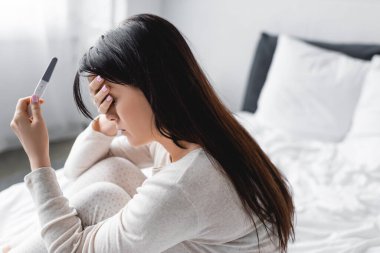 Hayal kırıklığına uğramış bir kadın hamilelik testi tutuyor ve yatak odasında negatif sonuç veriyor. 
