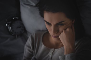 Uykusuzluk çeken üzgün bir kadının çalar saatin yanında yatışı. 