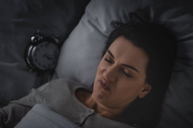 Uykusuzluk çeken ve alarm saatinin yanında yatan hoşnutsuz kadın manzarası. 