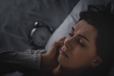 Uykusuzluk sorunu olan, alarmlı saatin yanında yatan bir kadının seçici odağı. 