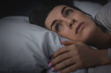 selective focus of displeased woman having insomnia while lying on bed at night  clipart