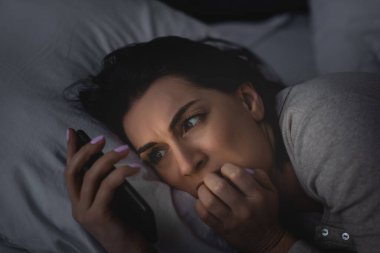 Yatak odasında akıllı telefon kullanan uykusuzluk çeken korkmuş bir kadın. 