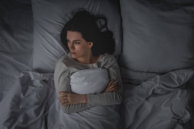 Uyku bozukluğu olan ve kollarını kavuşturup yatak odasında yatan bir kadın. 