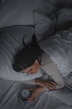 Uyku bozukluğu olan bir kadın yatak odasındaki çalar saate bakıyor. 
