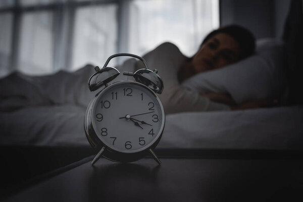 selective focus of alarm clock on bedside table near awake woman 