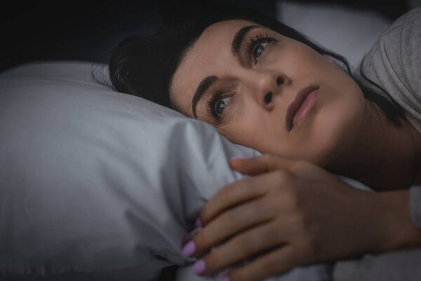 selective focus of displeased woman having insomnia while lying on bed at night 