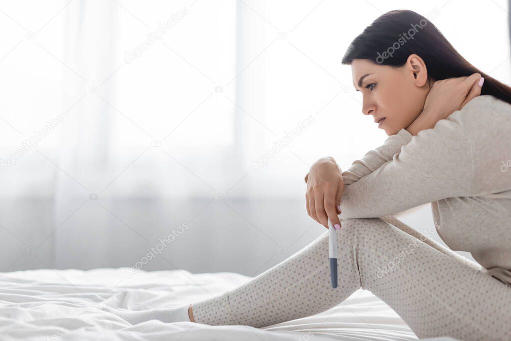 side view of sad woman holding pregnancy test with negative result 