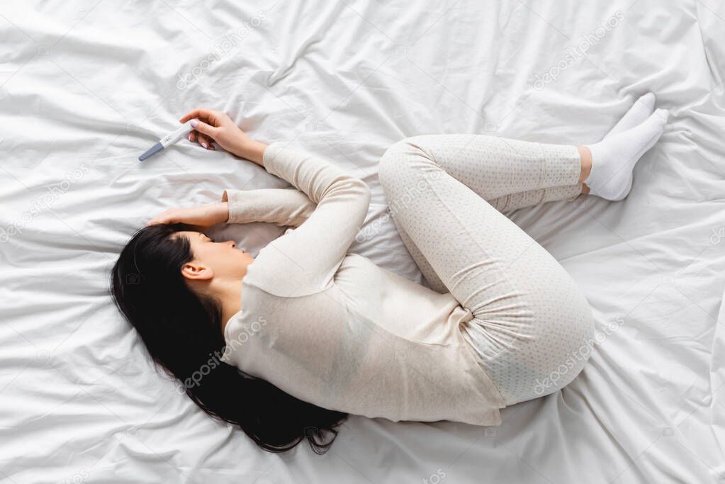 top view of depressed woman lying on bed near pregnancy test with negative result 