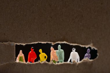 Selective focus of cardboard with hole and people figures isolated on black, concept of social equality clipart