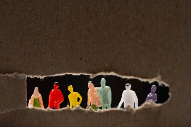 Selective focus of cardboard with hole and people figures isolated on black, concept of social equality clipart