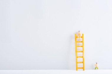 Two people figures with ladder on white surface on grey background, concept of equality rights  clipart