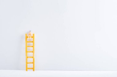 Doll on ladder on white surface on grey background, concept of equality rights  clipart