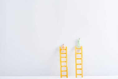 Plastic people figures on ladders on white surface on grey background, concept of equality rights  clipart