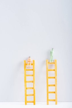 Two people figures on ladders on white surface on grey background with copy space, concept of equality rights  clipart
