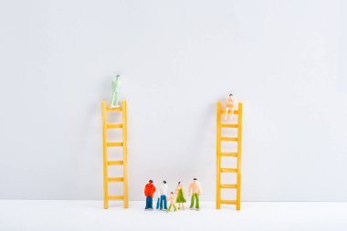 Dolls on ladders with people figures on white surface on grey background, concept of equality rights  clipart
