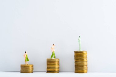 Gri arkaplandaki beyaz yüzeydeki madeni paralar üzerindeki sıra insan figürleri, finansal eşitlik kavramı