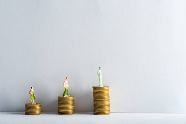 Gri arka planda beyaz yüzeyde altın sikkeler üzerine üç kişi, finansal eşitlik kavramı