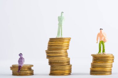 Gri, finansal eşitlik kavramına izole edilmiş beyaz yüzeydeki istiflenmiş madeni paraların üzerindeki insan figürlerine yakından bakın.