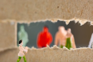 Selective focus of toy near hole in cardboard with silhouettes of people figures at background clipart
