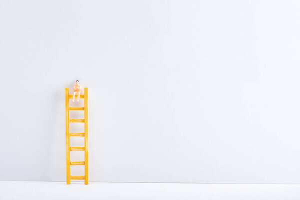 Doll on ladder on white surface on grey background, concept of equality rights 