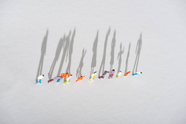 Top view of row of plastic people figures on white surface with shadow