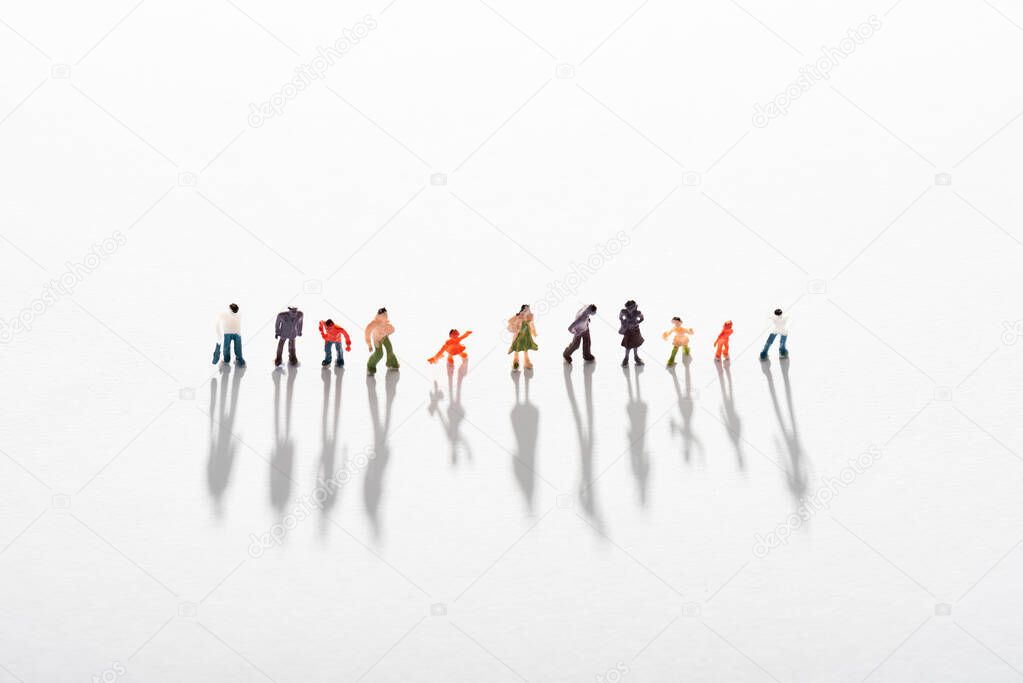 High angle view of row of plastic people figures with shadow on white surface