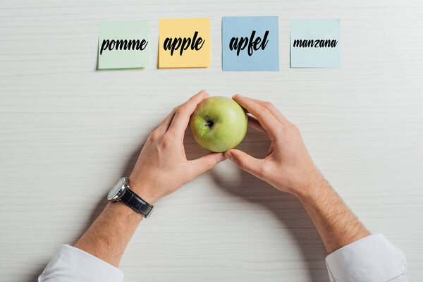 cropped view of businessman holding apple on table with sticky notes with apple translation