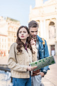 Znepokojená a pozorná dívka drží mapu a dívá se jinam s přítelem ve městě